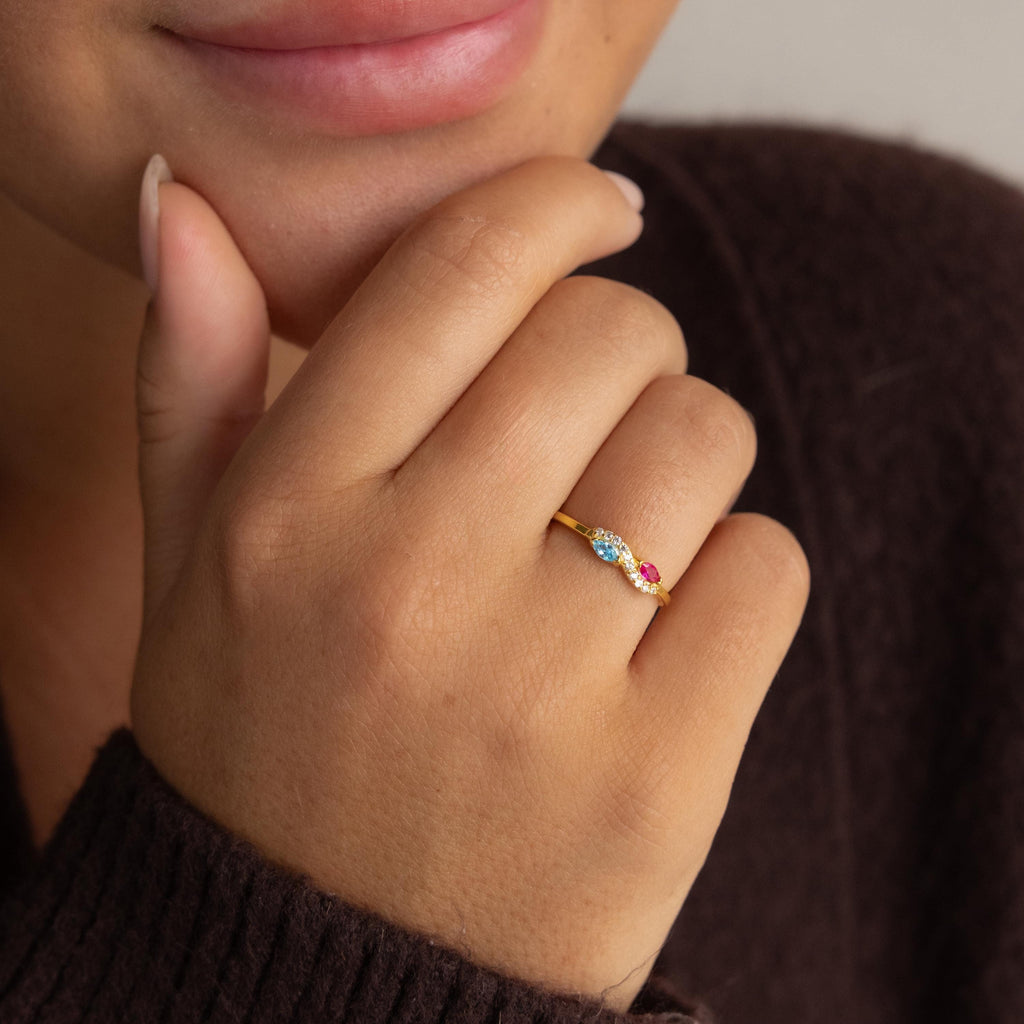 Someone touches their chin while wearing the Infinity Marquise Birthstone Ring, which features blue, white, and pink stones.