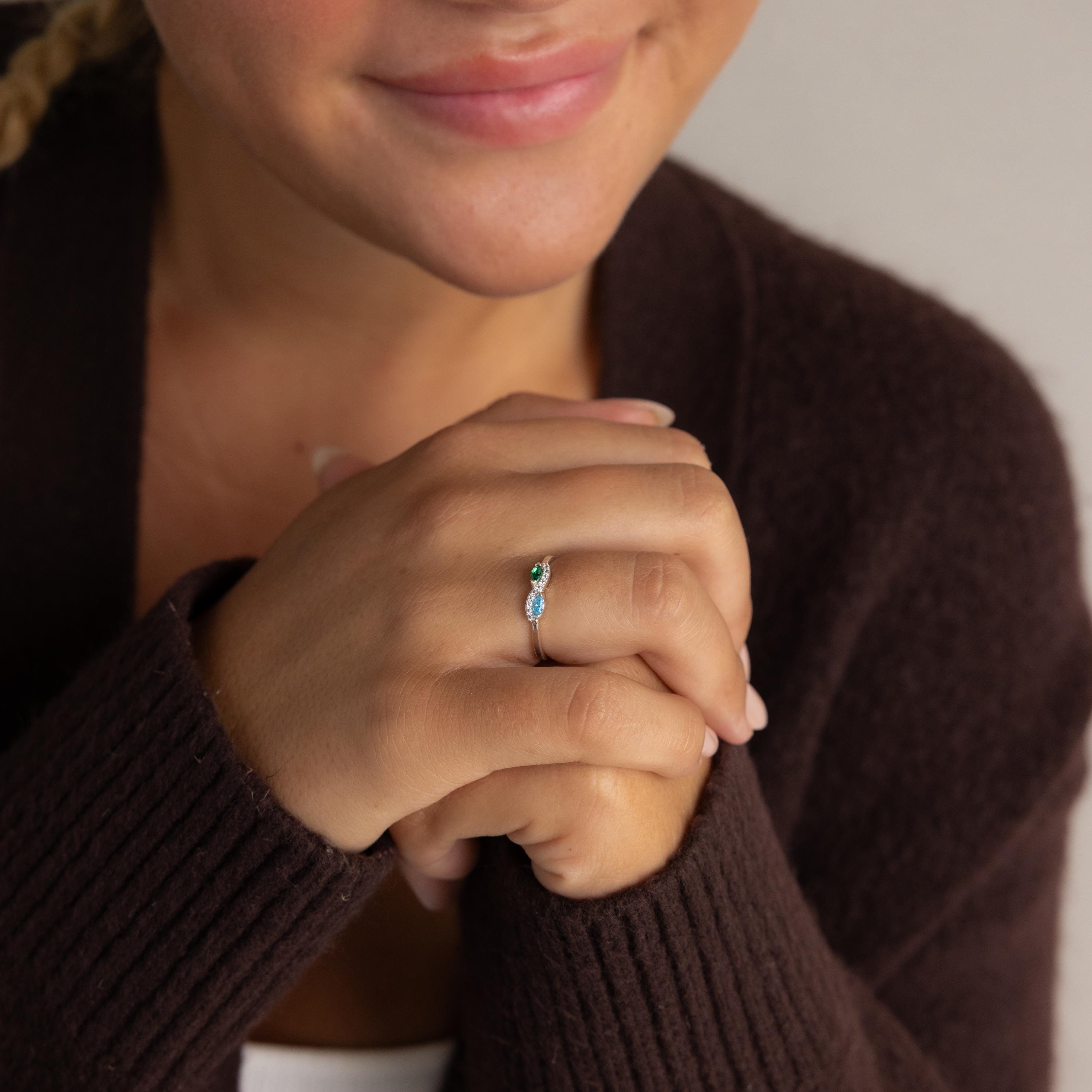 A smiling woman in a dark sweater displays her Infinity Marquise Birthstone Ring, featuring a striking blue marquise-cut stone, on her finger.