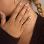A hand with nude polished nails, wearing a Multiple Baguette Birthstone Ring, gently touches the face near a braided hairstyle.