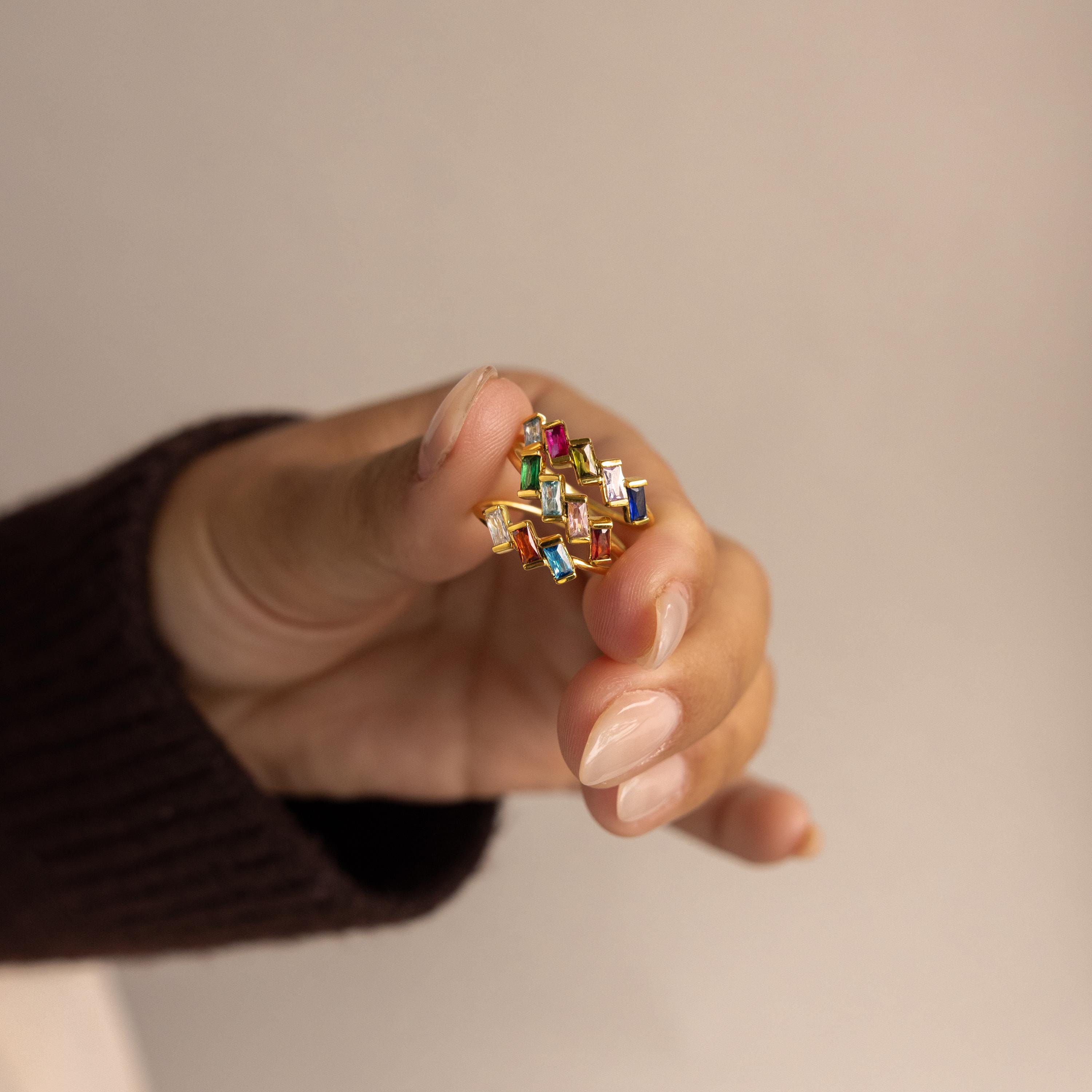 A hand displays the Multiple Baguette Birthstone Ring, featuring vibrant rectangular gemstones, against a neutral background.