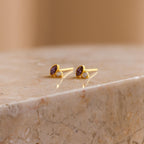 Diamond Marquise Birthstone Studs featuring purple and clear gemstones are displayed on polished marble. These marquise-cut earrings bring an elegant touch to any look.