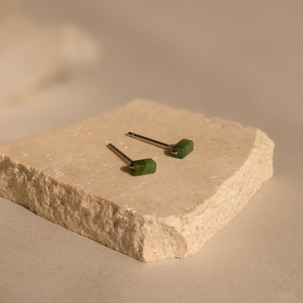 The Jade Bar Jewelry Set in Sterling Silver features two earrings with green rectangular stones, displayed on a textured beige stone slab.