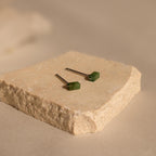 The Jade Bar Jewelry Set in Sterling Silver features two earrings with green rectangular stones, displayed on a textured beige stone slab.