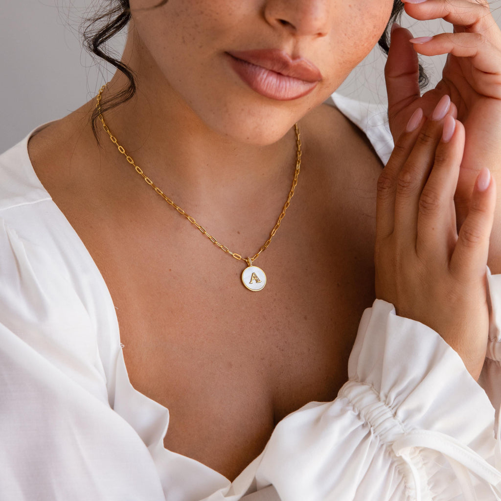 Woman in a white blouse wearing a Gemstone Initial Disc Necklace featuring a round gold pendant with the letter A.