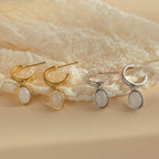 Two pairs of Moonstone Drop Hoops—one gold, one silver—are displayed on lace fabric, capturing the timeless elegance typical of celestial-inspired jewelry.