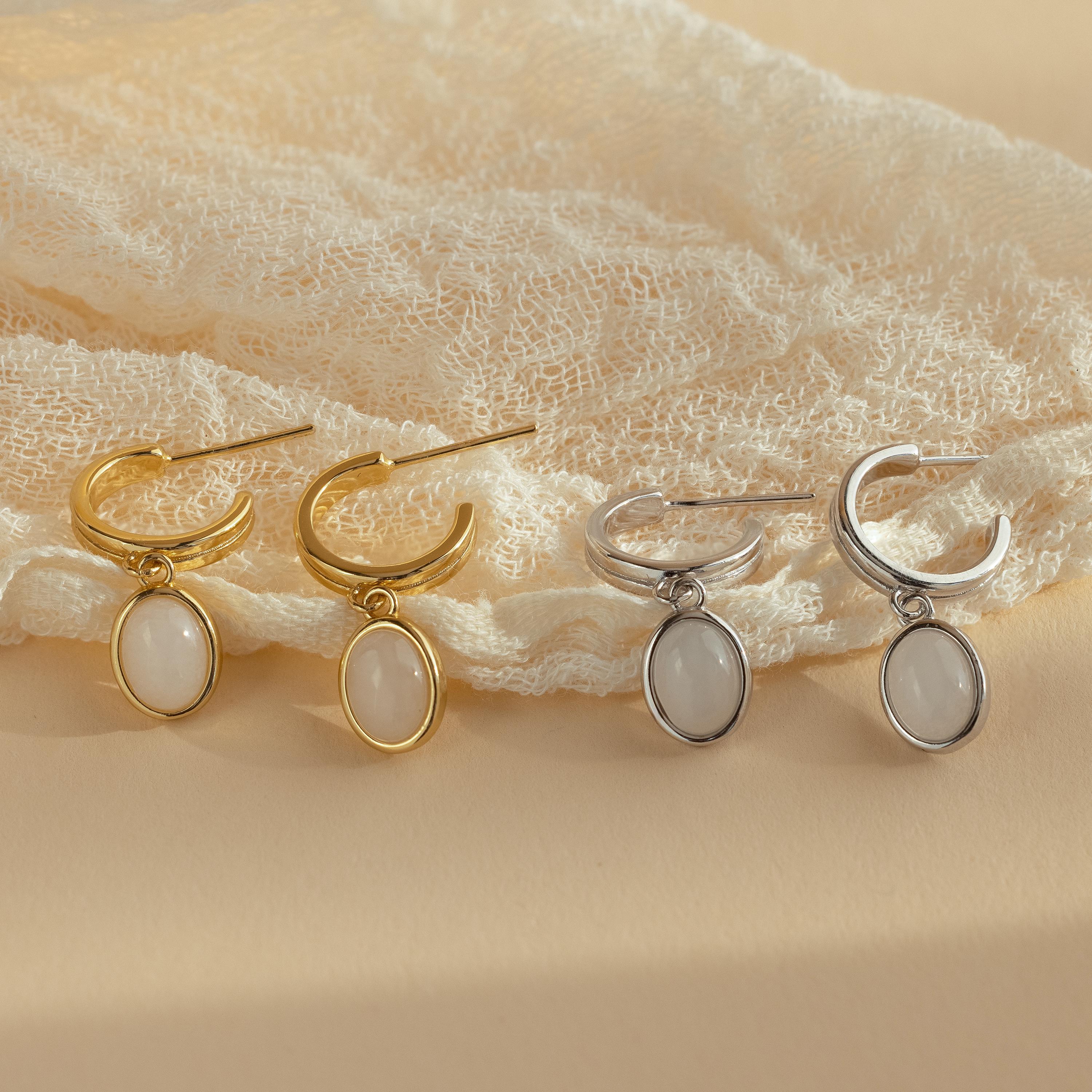 Two pairs of Moonstone Drop Hoops—one gold, one silver—are displayed on lace fabric, capturing the timeless elegance typical of celestial-inspired jewelry.