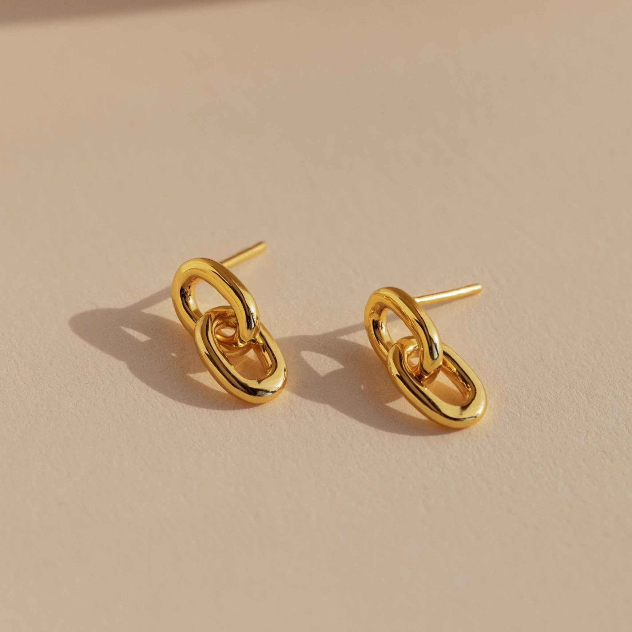 Link Drop Studs are shown on a beige surface with soft lighting, highlighting their elegant chain link design and casting delicate shadows.