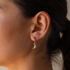 A close-up of a woman’s ear wearing a crescent moon-shaped earring from the Opal Sun & Moon Huggies collection—a delicate silver accessory perfect for fans of celestial jewelry.