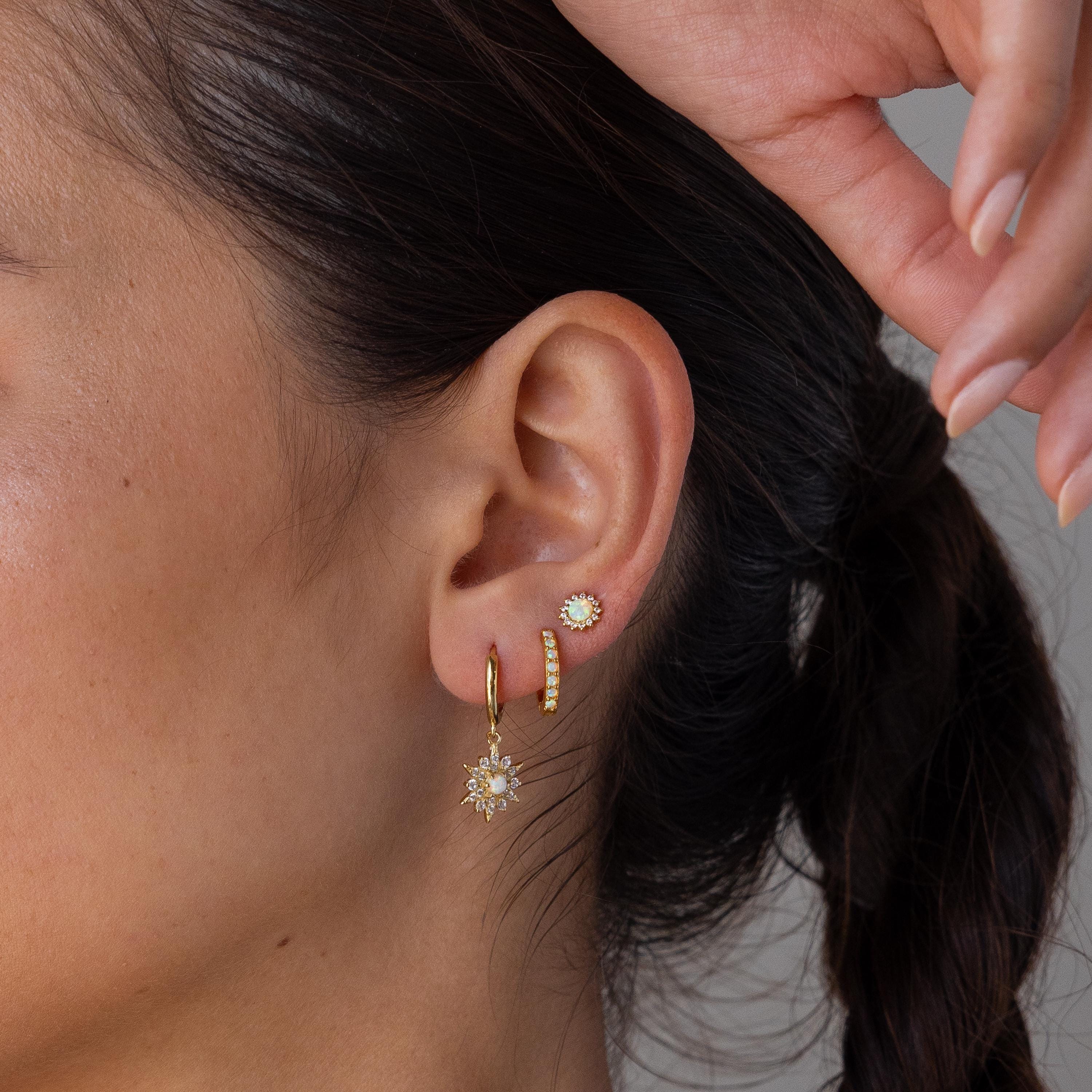 Close-up of a woman's ear wearing Opal Sun & Moon Huggies, with mismatched gold earrings—a sun-shaped dangle and two studs—creating a cosmic jewelry vibe.