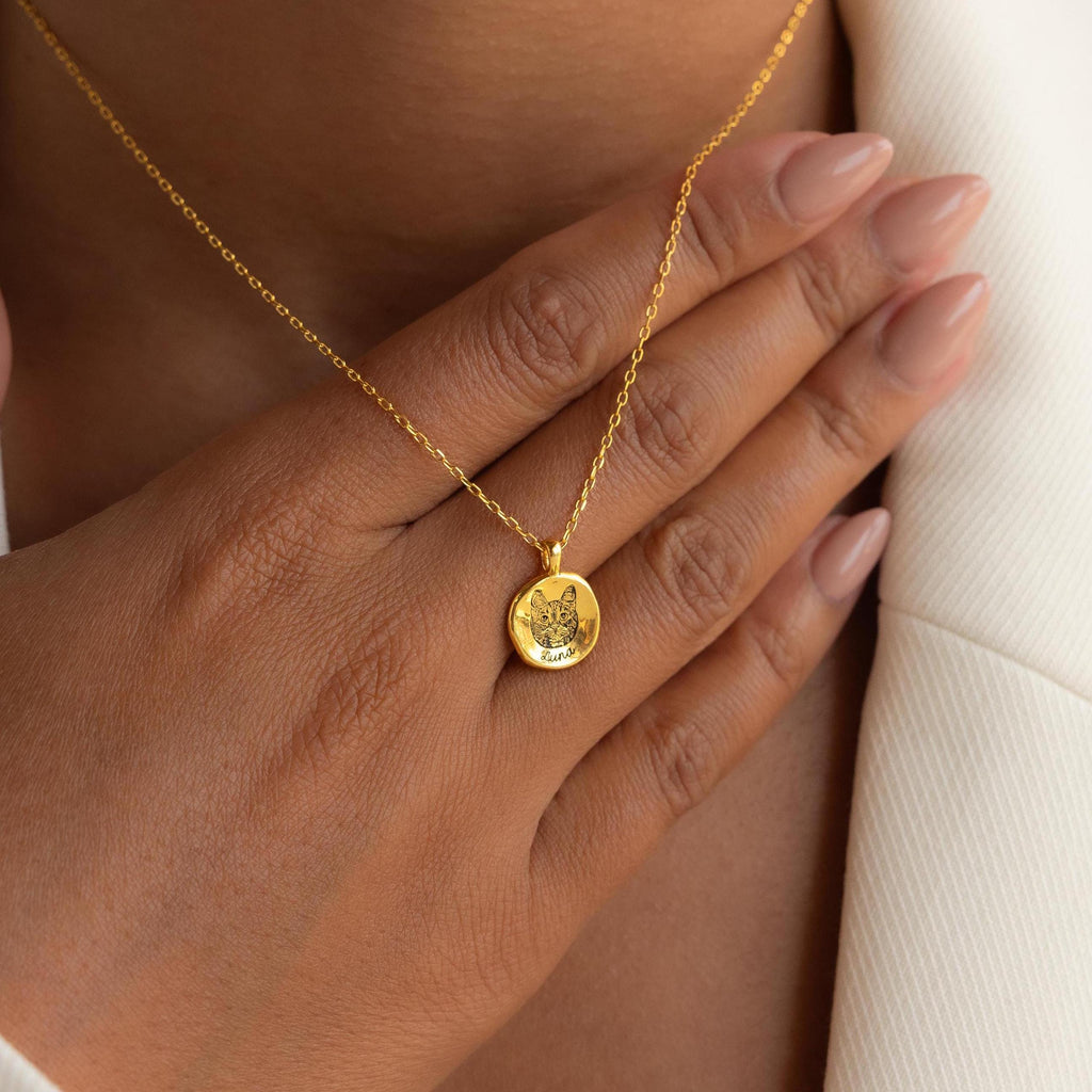 A hand with nude nails rests on the chest, showcasing the Pet Portrait Coin Necklace, a gold piece engraved with a lion—ideal custom jewelry for pet lovers.