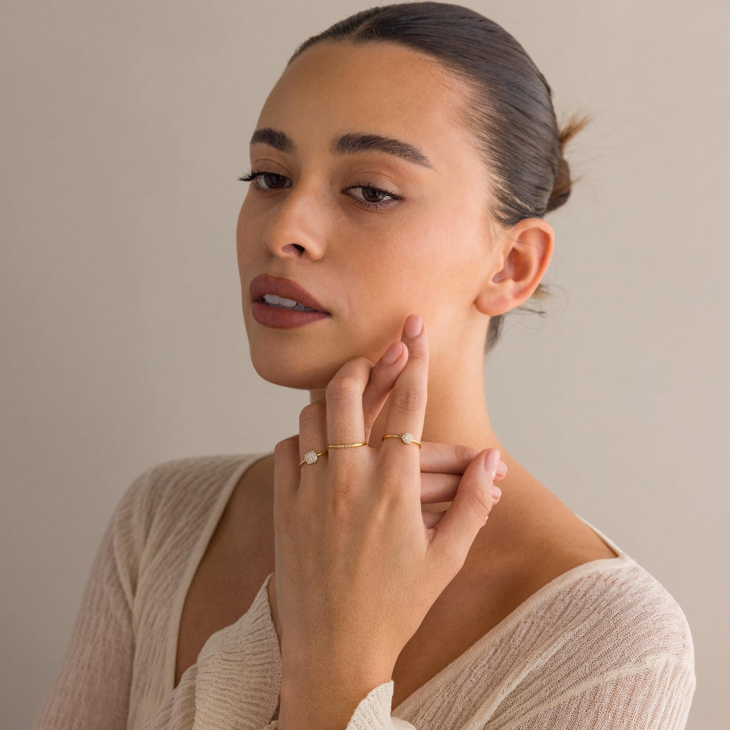 A woman with hair in a bun wears a cream knit top and the Classic Pave Ring Set in gold, elegantly posing with her hand near her face to showcase the jewelry.