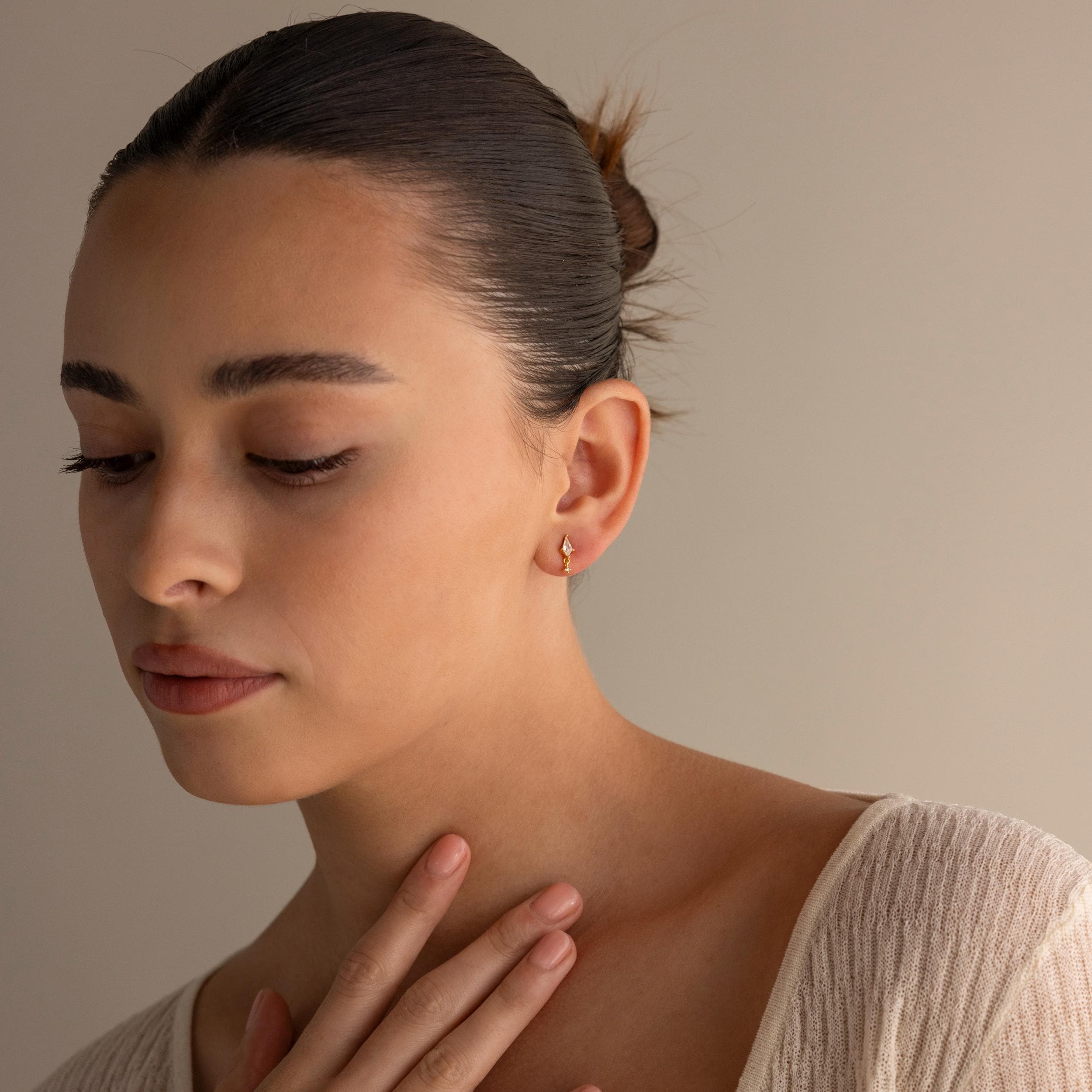 Woman with dark hair in a bun, wearing a cream sweater and Diamond Kite Drop Earrings, exudes vintage charm as she looks down with her hand on her chest.
