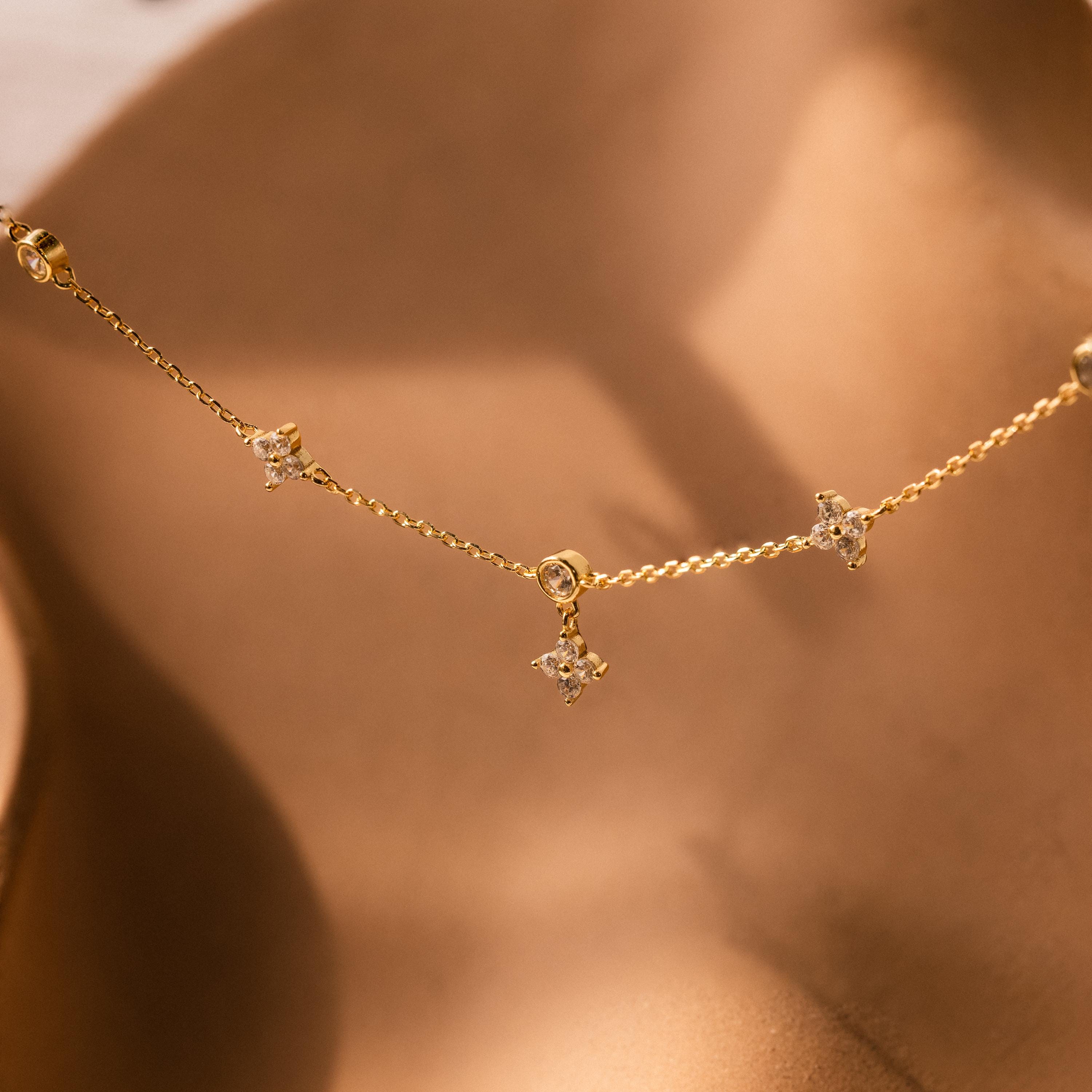 The Ivy Diamond Station Necklace features a gold chain adorned with delicate diamond stations, shown against a soft beige background.