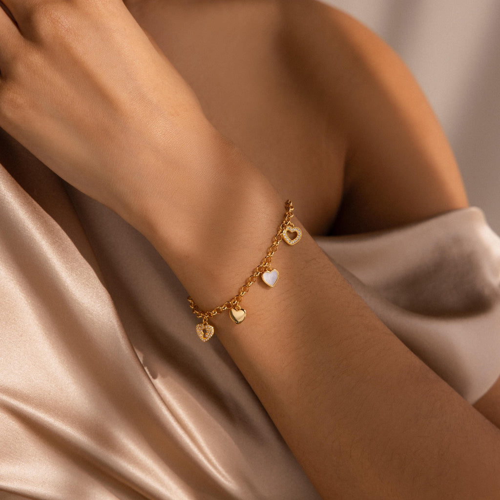 A womans arm adorned with the Heart Charm Bracelet in gold, draped in champagne satin—an elegant gift for your girlfriend.