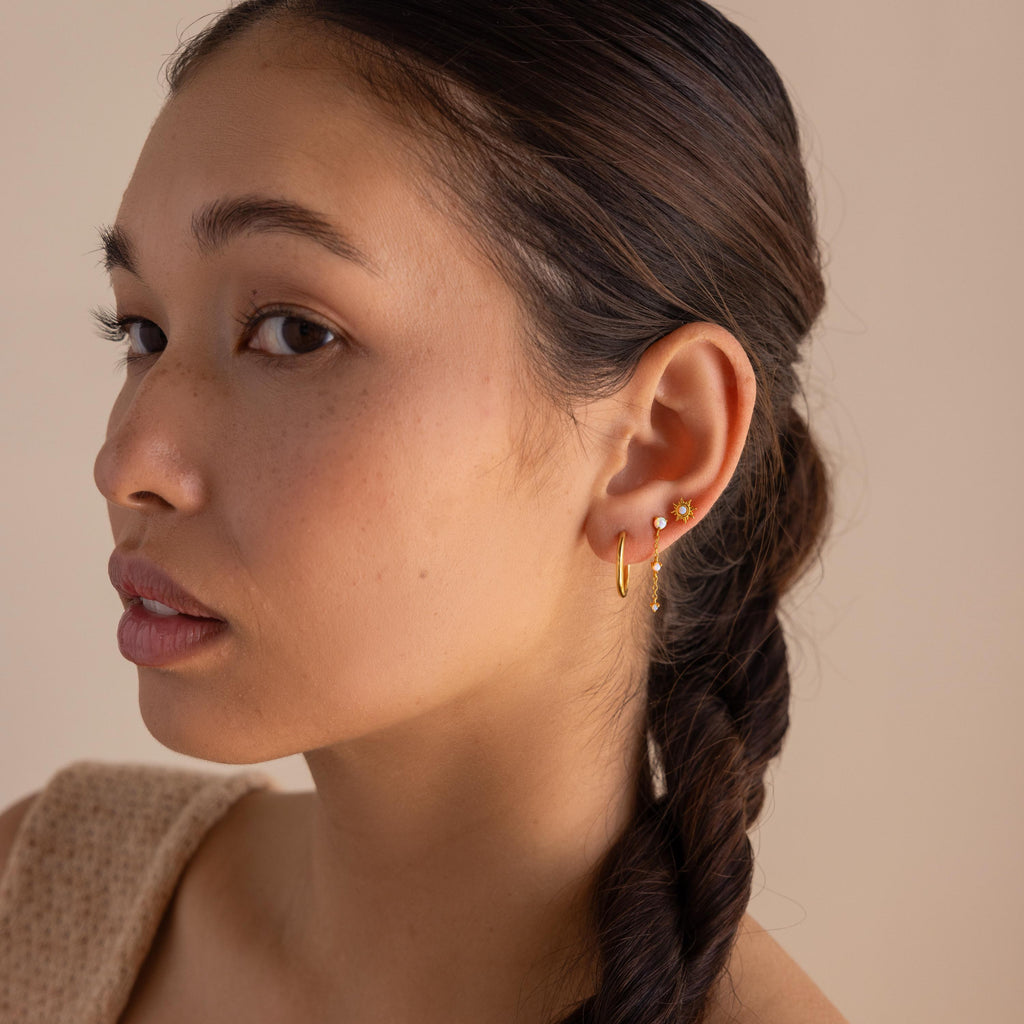A woman with braided hair wears multiple gold earrings, including celestial jewelry and Opal Sun Flat Back Studs, as she looks to the side against a neutral background.