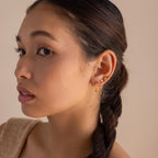A woman with braided hair wears multiple gold earrings, including celestial jewelry and Opal Sun Flat Back Studs, as she looks to the side against a neutral background.