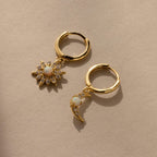 The Opal Sun & Moon Huggies feature two gold hoop earrings—one with a sunburst, one with a crescent charm—both adorned with white stones for a chic, celestial touch.