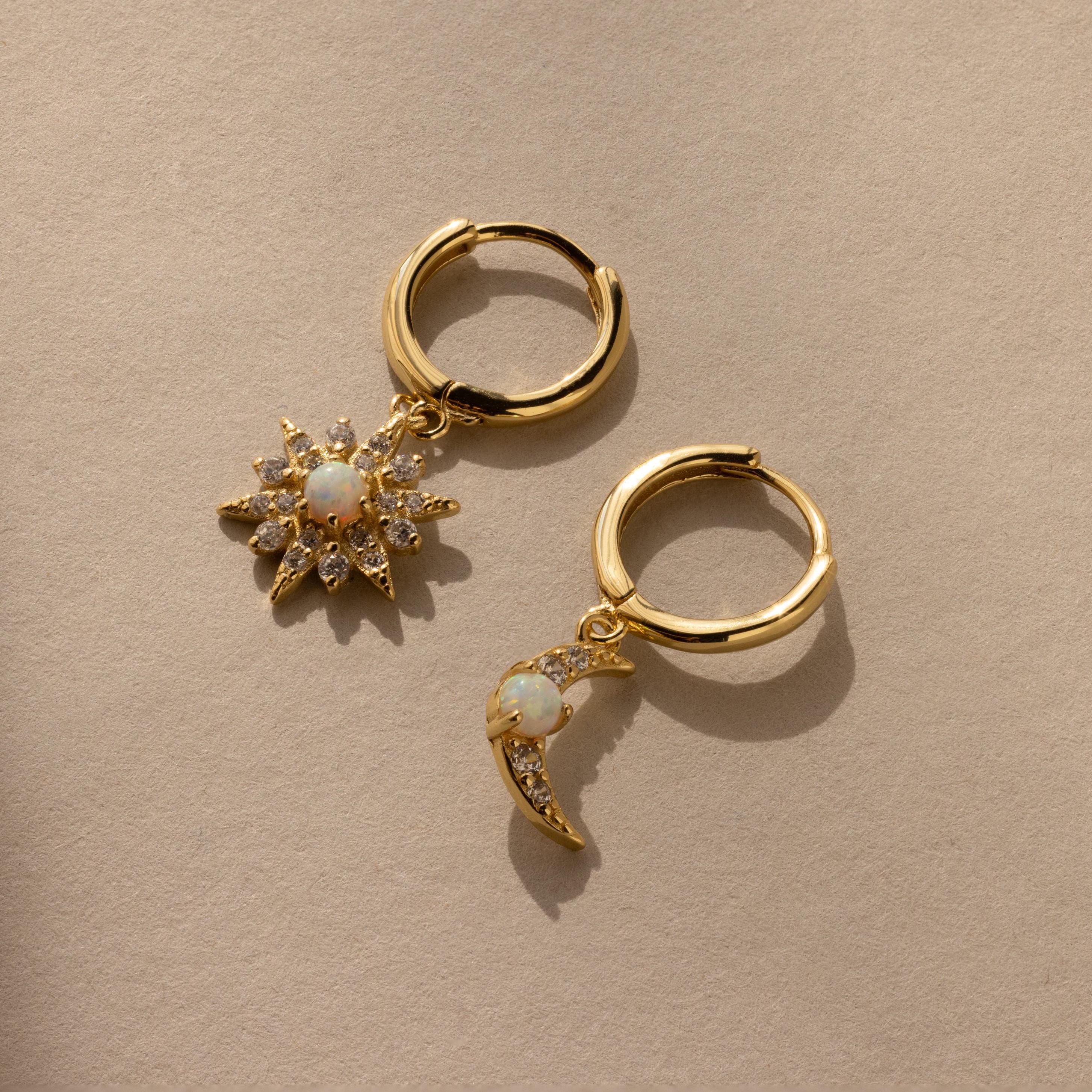 The Opal Sun & Moon Huggies feature two gold hoop earrings—one with a sunburst, one with a crescent charm—both adorned with white stones for a chic, celestial touch.