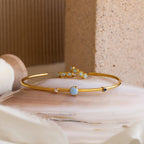 Blue Opal Beaded Huggies paired with gold bangles adorned with opal and blue gemstones, displayed on a polished stone surface against a neutral background.