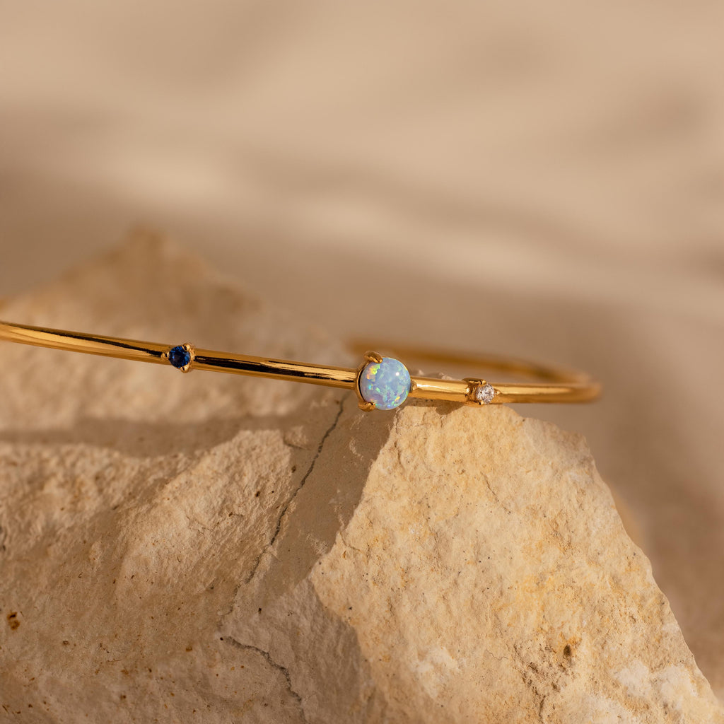 An elegant Opal & Diamond Cuff Bracelet, featuring delicate opals and sparkling diamonds, rests on a light-colored stone.
