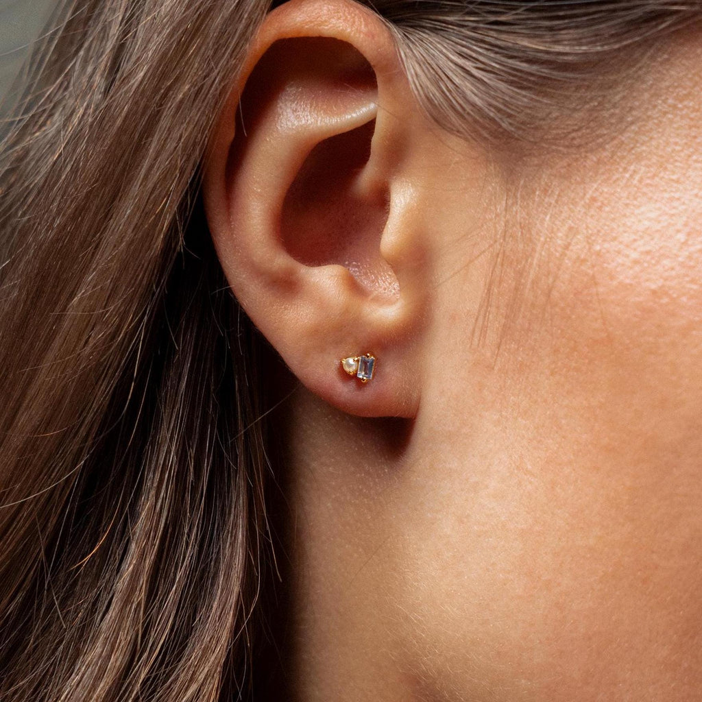 Close-up of a woman’s ear adorned with Pearl Aquamarine Studs, featuring small gold settings and sparkling aquamarine gems for a subtle, elegant touch.
