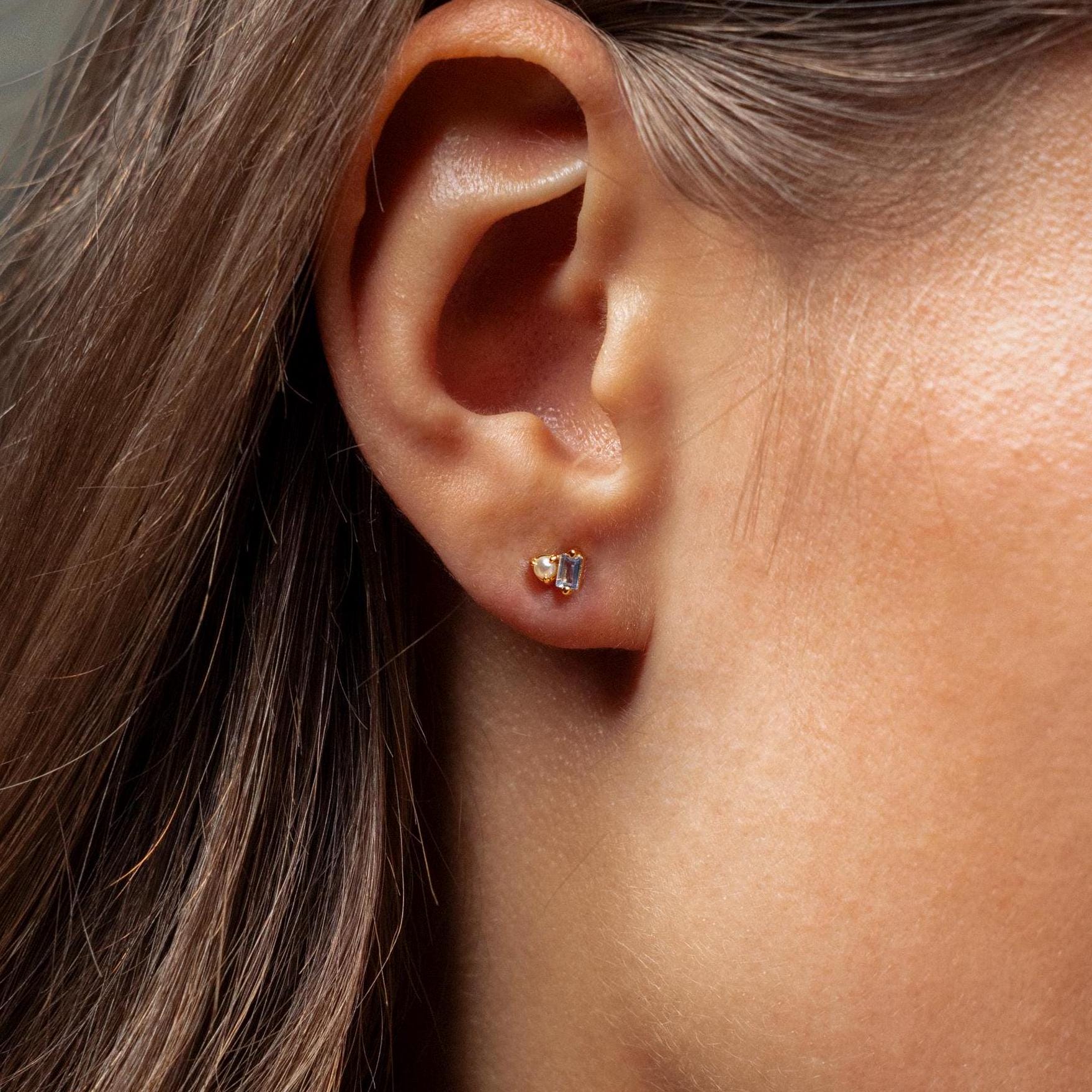 Close-up of a woman’s ear adorned with Pearl Aquamarine Studs, featuring small gold settings and sparkling aquamarine gems for a subtle, elegant touch.
