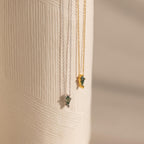 Two Agate Art Deco Pendant Necklaces—one silver, one gold—feature striking green moss agate pendants and hang elegantly against a textured white surface.