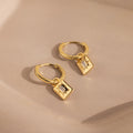 Art Deco Diamond Tag Huggies: Gold vintage-inspired hoops featuring square, diamond-accented charms set against a soft beige background.