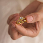 A hand displays the Vintage Diamond Rings Set, featuring a gold ring with a round diamond, leaf accents, and a marquise-detailed band.