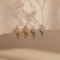 Two pairs of small, flower-shaped earrings, including delicate Butterfly Drop Huggies in gold and silver, are displayed on textured beige paper.