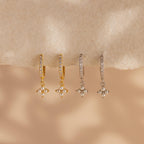 Two pairs of Pearl Ivy Flower Huggies—one gold, one silver—feature small pearl cluster charms resembling delicate florals, displayed on a beige surface.