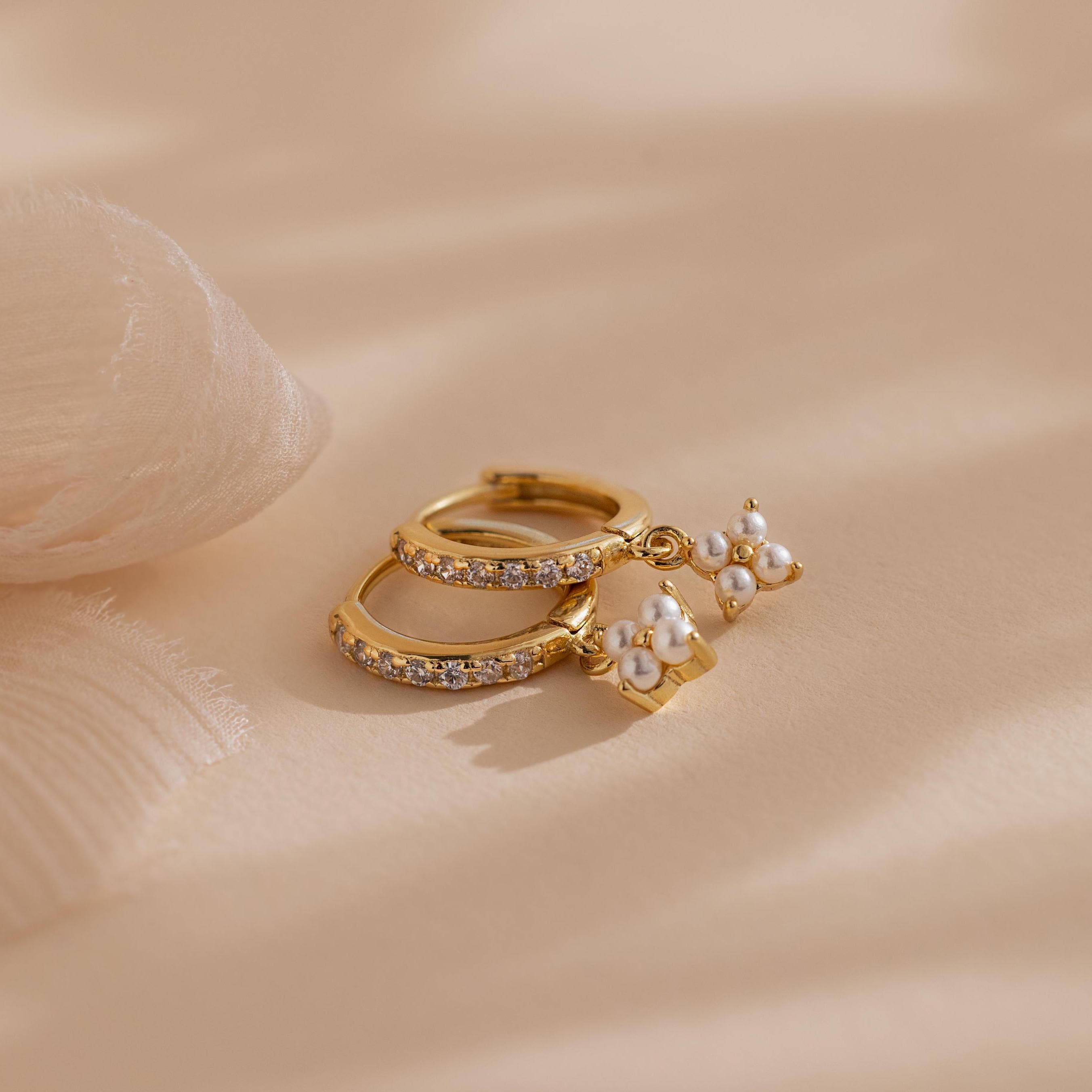 Pearl Ivy Flower Huggies in 18K Gold, featuring small white pearls and crystals in a floral design, displayed on a soft beige fabric background.