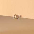 The Dainty Pave Earrings Set, featuring three gold hoop earrings and a dangling diamond-accented earring, is beautifully displayed on a beige background.