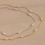 The Hali Pearl Station Necklace, available in silver and gold with small white pearls, highlights minimalist elegance against a beige backdrop.