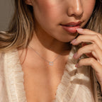 A woman touches her chin gently while wearing a ruffled cream blouse and the Diamond Sun Necklace, a delicate sunburst pendant.