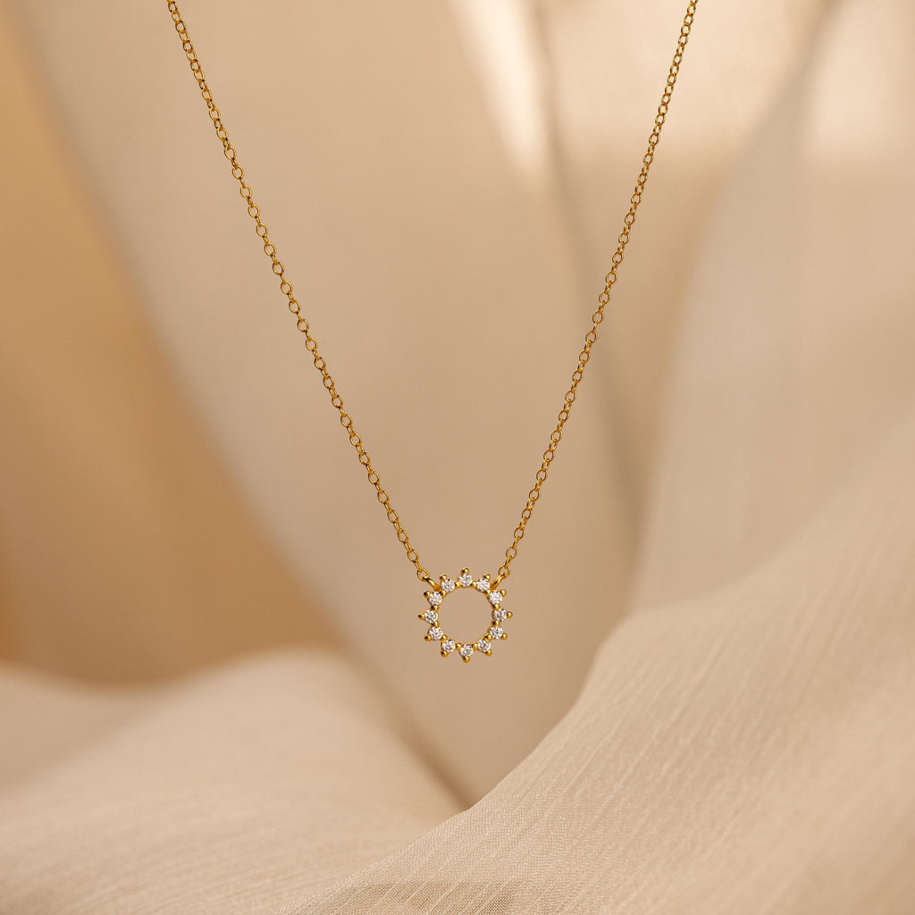 Diamond Sun Necklace with a radiant sunburst pendant set with sparkling diamonds, elegantly displayed against a soft beige fabric background.