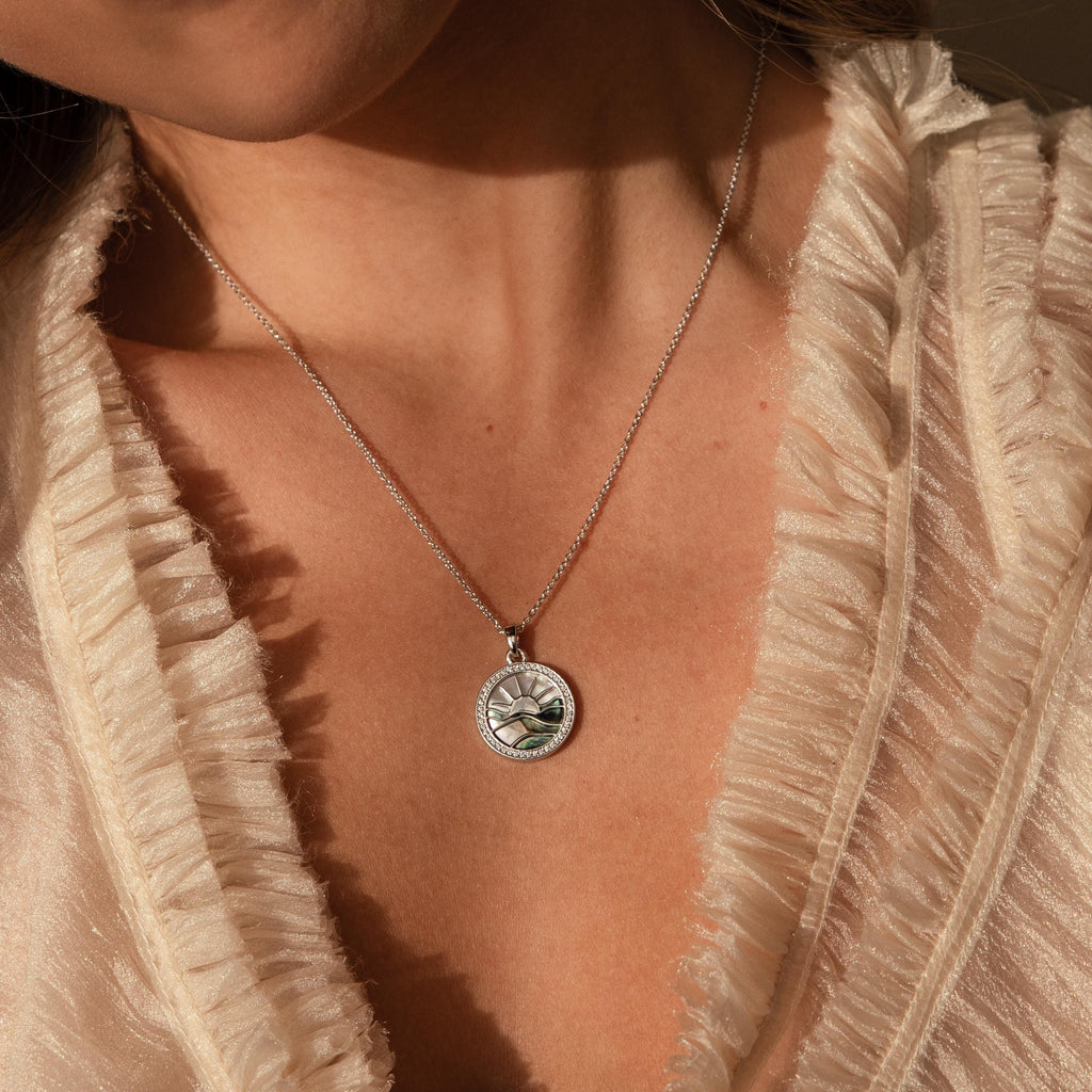 Close-up of a woman wearing the Abalone Sunrise Pendant Necklace in White Gold, featuring abalone and pearl gemstones, styled with a cream ruffled blouse.