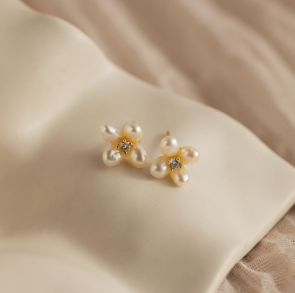 The Pearl Flower Studs are displayed on a white pillow, highlighting the elegance and floral inspiration of these earrings.