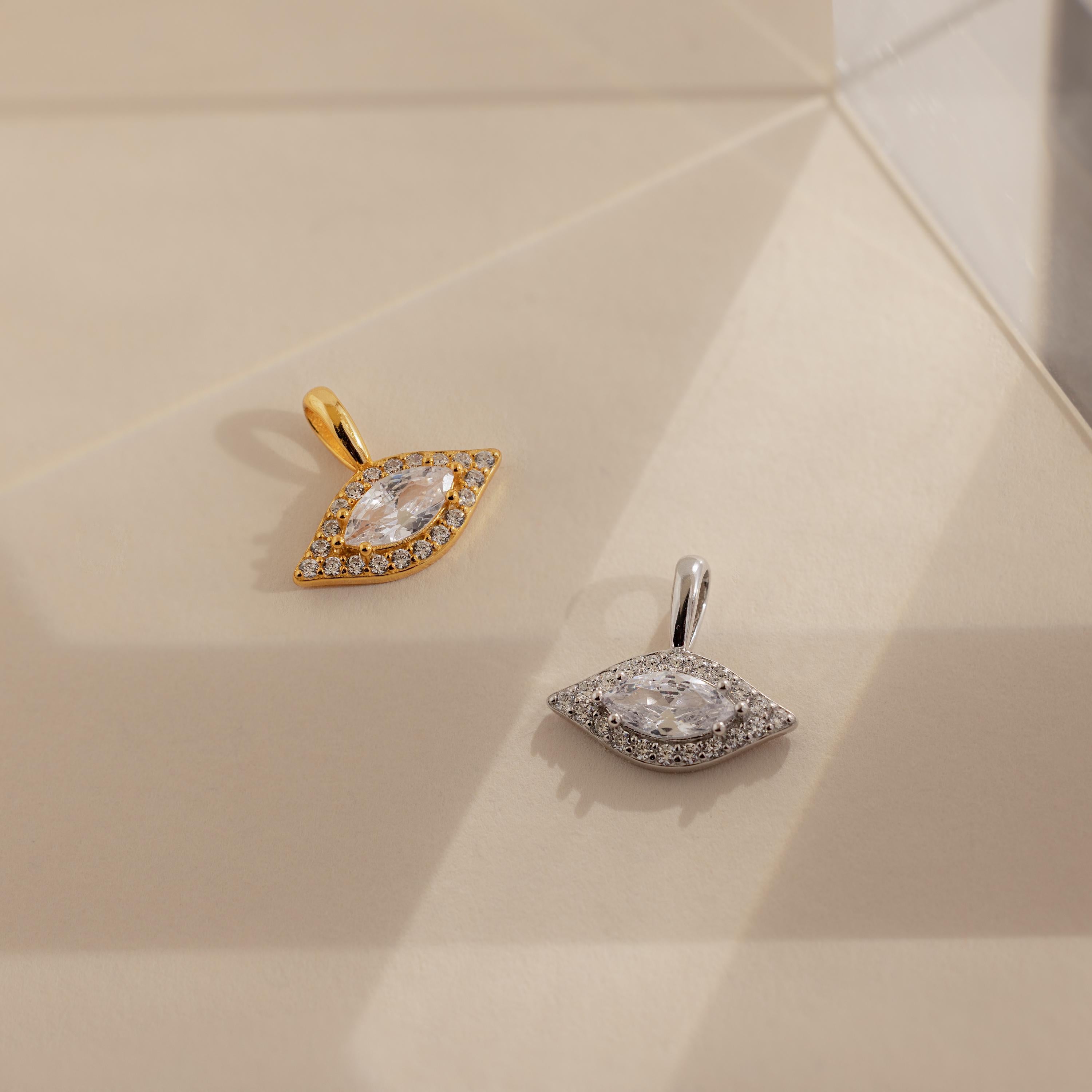 One gold and one silver Pave Evil Eye Charm laying side by side