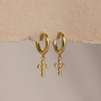 Opal Cross Huggies: gold huggie earrings with iridescent opal cross charms, shown on textured paper.