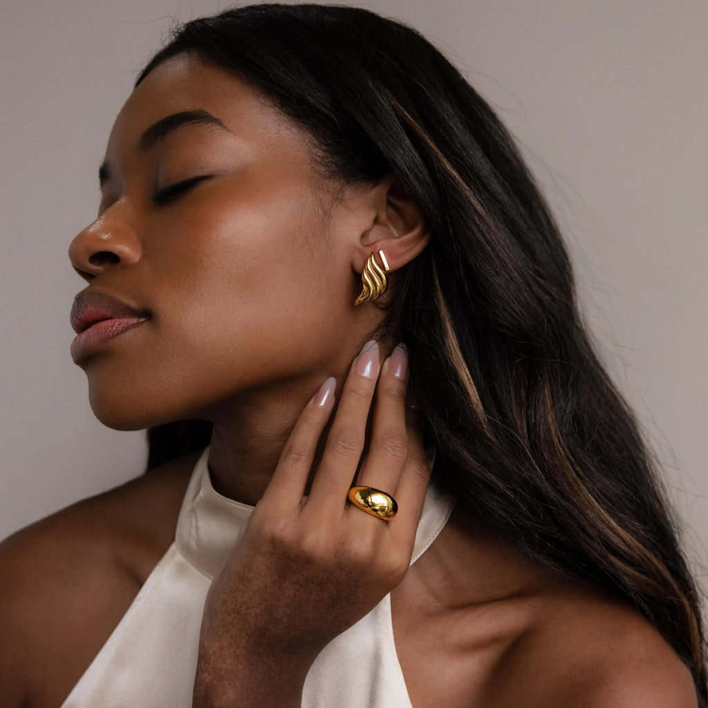 Woman with long hair wears Bold Wing Studs earrings and a ring, eyes closed, dressed in a light halter top.
