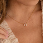 The Diamond Sun Necklace features a sunburst pendant with sparkling diamonds, elegantly worn on a woman's neck paired with a ruffled top.