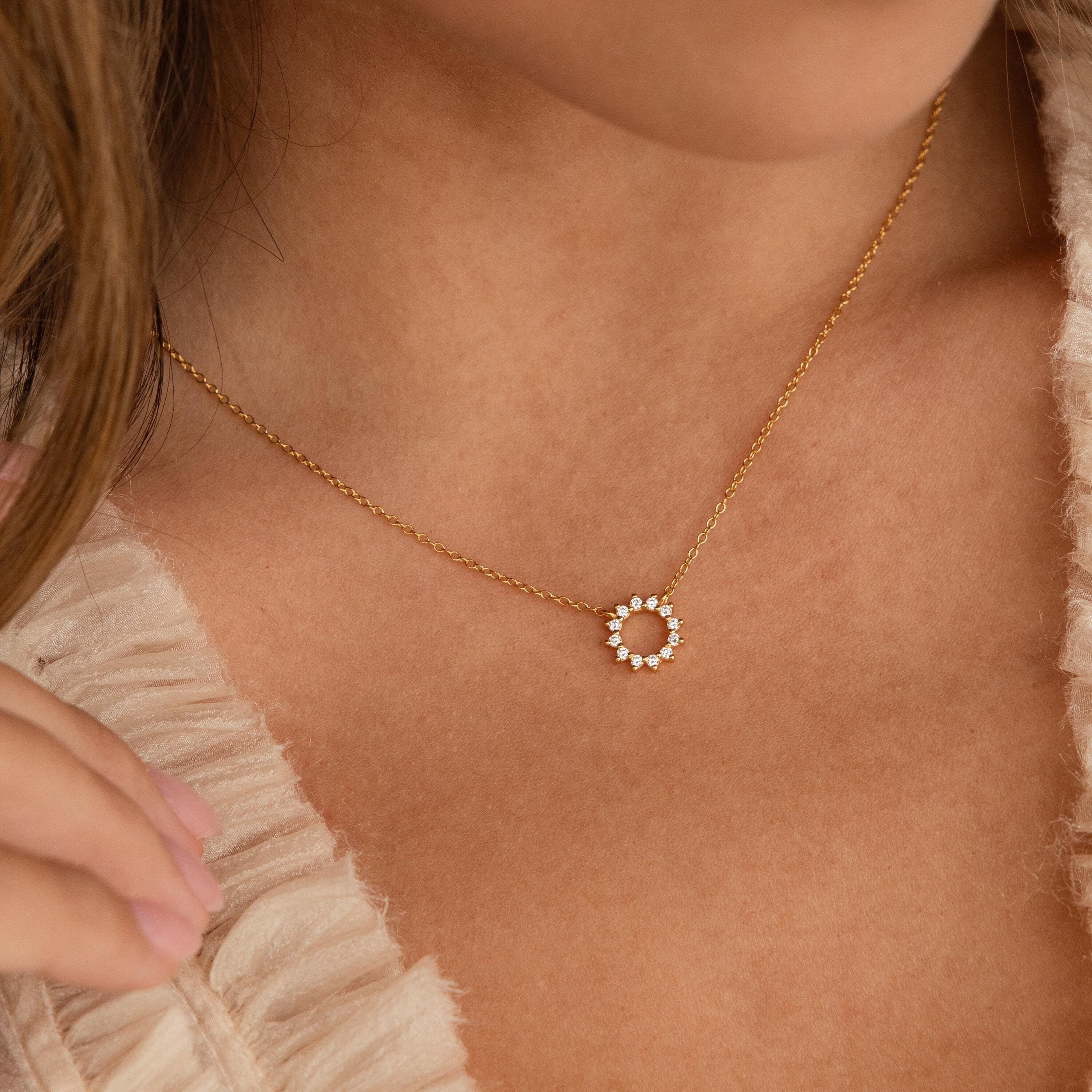 The Diamond Sun Necklace features a sunburst pendant with sparkling diamonds, elegantly worn on a woman's neck paired with a ruffled top.