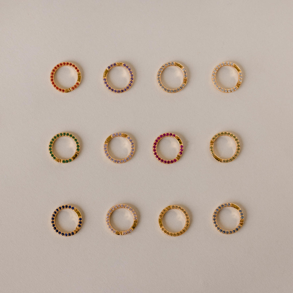 A Pave Pink Tourmaline Charm Clip, set with vibrant pink gemstones, shines against a beige backdrop—a personalized jewelry piece perfect for expressing your unique style.