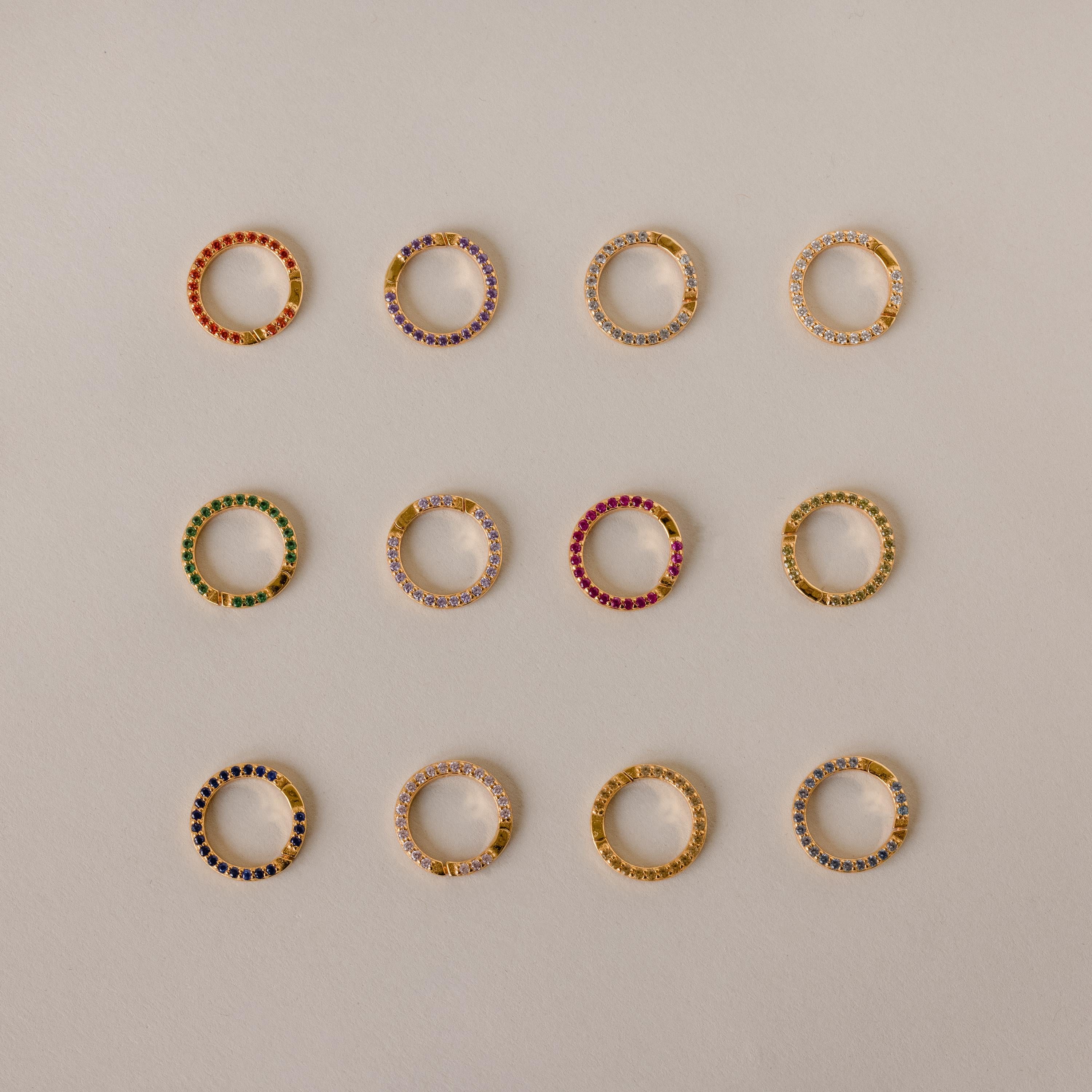 A Pave Pink Tourmaline Charm Clip, set with vibrant pink gemstones, shines against a beige backdrop—a personalized jewelry piece perfect for expressing your unique style.