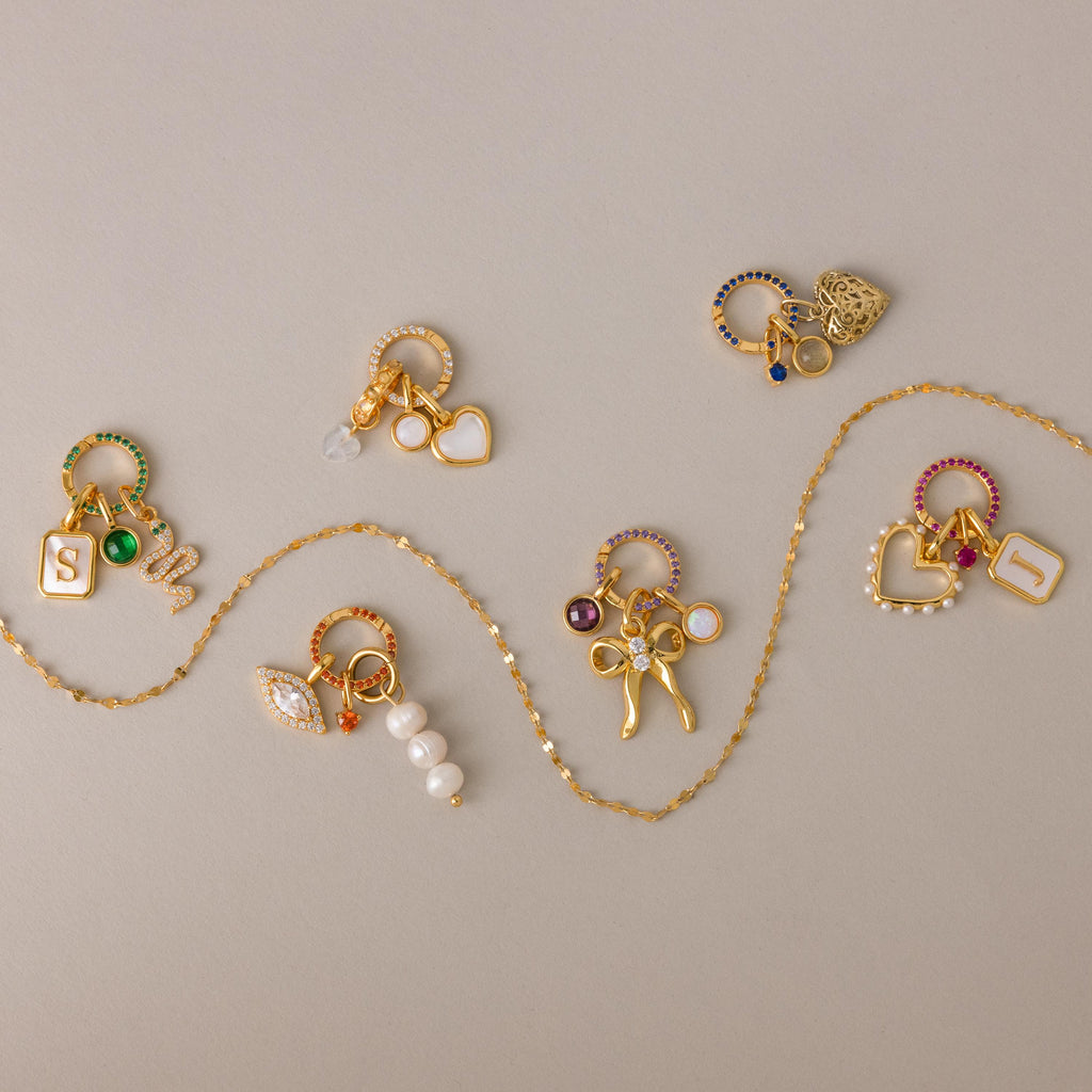 The Pave Birthstone Charm Clip, featuring colorful gems, pearls, heart pendants, and a birthstone ring charm, is displayed on a neutral background—perfect for personalizing jewelry or adding to your favorite charm clip.