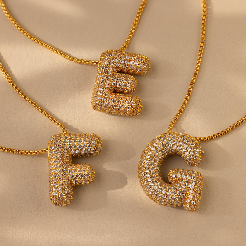 Three Pave Puff Letter Necklaces in 18K Gold, with sparkling pave diamond–studded letter pendants—E, F, and G—shine elegantly on a beige surface, each offering a dazzling gold charm for personalized luxury.
