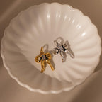 The Diamond Bow Charm in Sterling Silver, inspired by the coquette aesthetic, sparkles with CZ diamonds and crystals on a white scalloped dish.