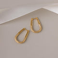 The Bold Pave Oval Hoops, featuring embedded pave diamonds, are displayed on a beige background with a white ribbon accent above.