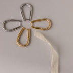 Four Bold Pave Oval Hoops are elegantly arranged like a flower on a light surface, with a textured strip as the stem.